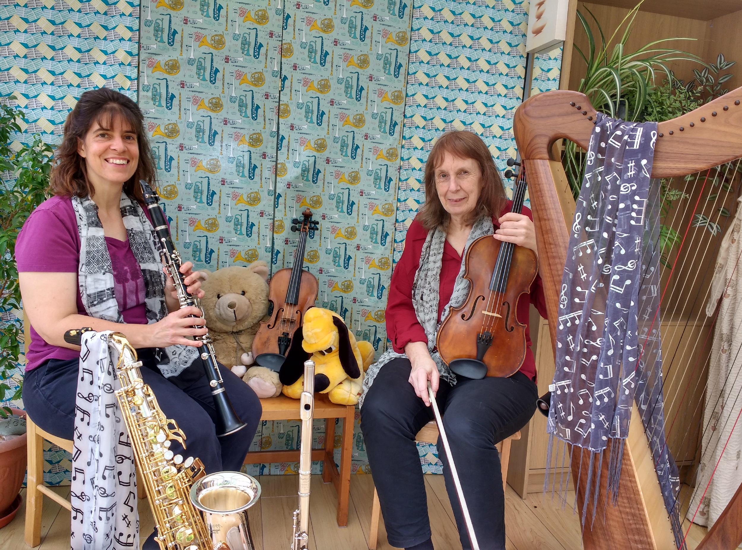 The two members of Chestra sit surrounded by instruments and light scarves. They have some teddies in the background.