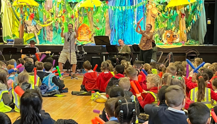 KS1 pupils participating in the little sing with boomwhakers with a band at the front.